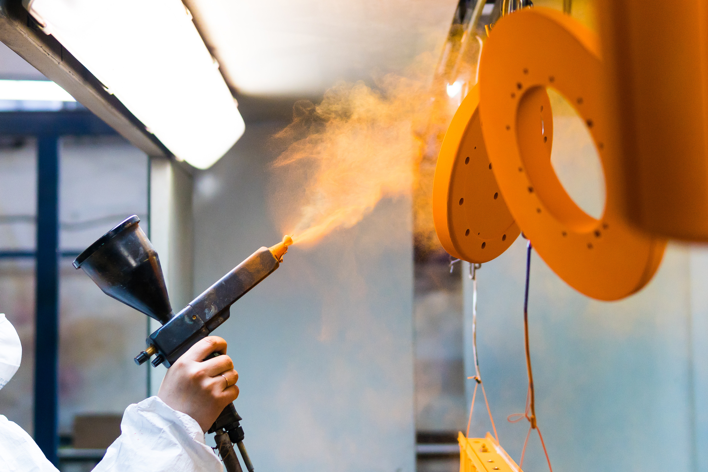 Powder coating of metal parts. A woman in a protective suit sprays powder paint from a gun on industrial equipment