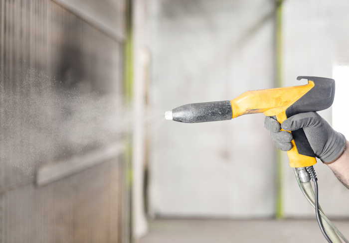 Detail of the hand of a man working in a factory finishing a job using the electrostatic powder coating technique with a spray gun.