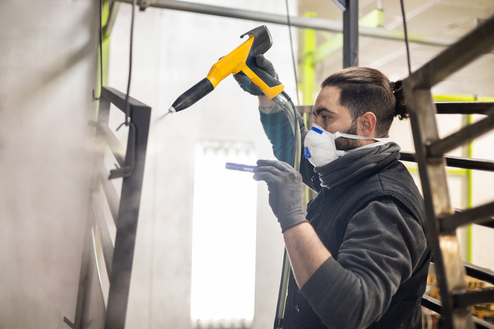 a man working in a factory finishes a job using the technique of electrostatic powder coating with a spray gun.